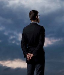 A business owner in a suit looking at a cloudy sky, representing the uncertainty and questions surrounding tax season.